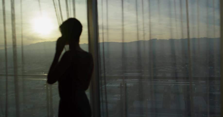 A woman talks on a phone in a hotel room at sunset