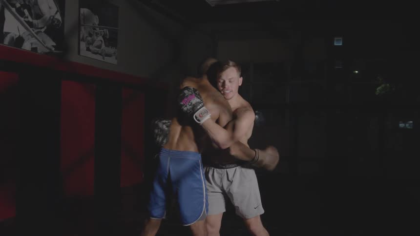 Two men wearing boxing gloves are hugging