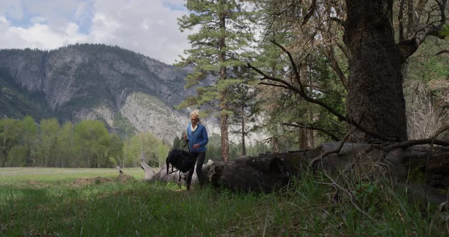 A woman sits on a fallen tree while hiking in mountains