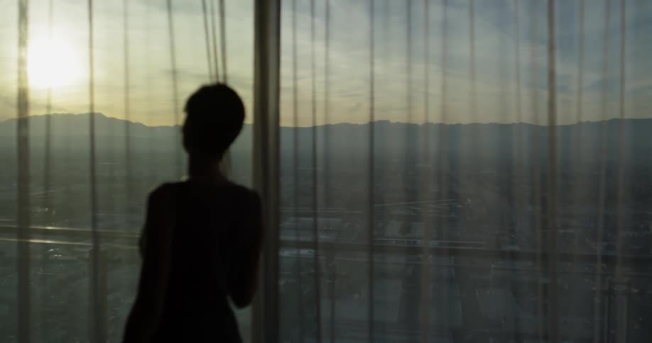 A woman stands behind the curtain at sunset