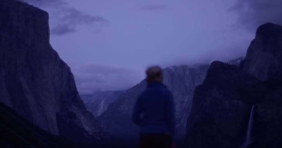 Person stands outside looking at cloud covered mountains