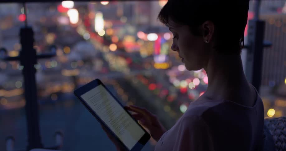 A woman scrolls on a tablet on a hotel balcony in las vegas