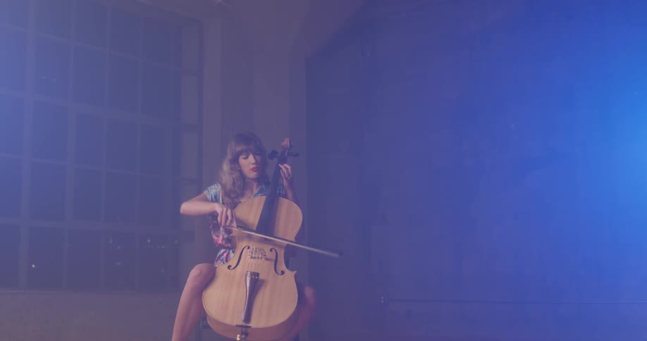 A woman plays a cello in a dim room