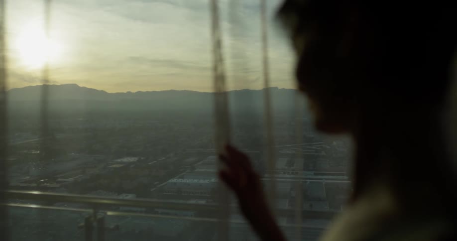 A woman looks out a hotel window at sunset