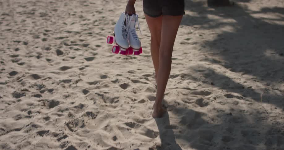 A woman walks barefoot while carrying roller skates