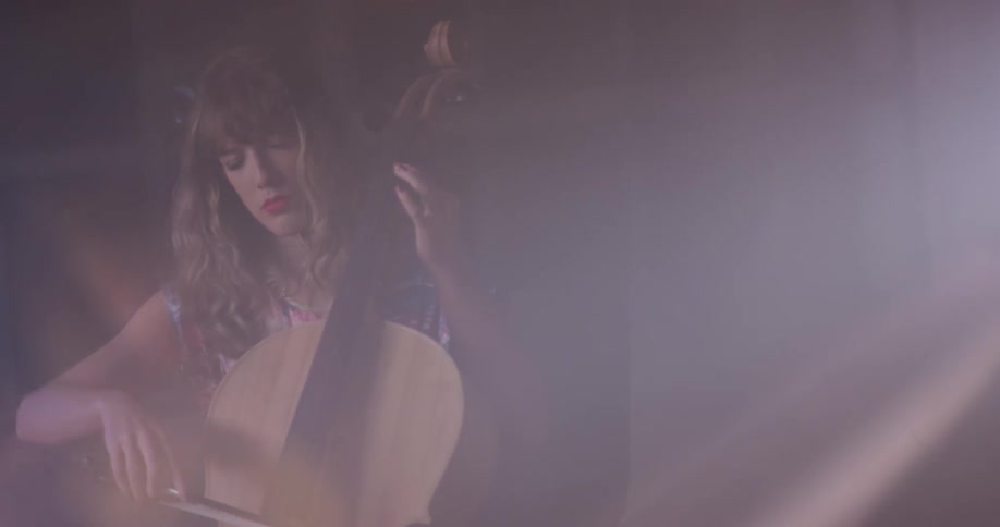A woman plays a cello in a dim room