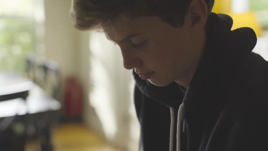 A teenage boy is deep in thought at home