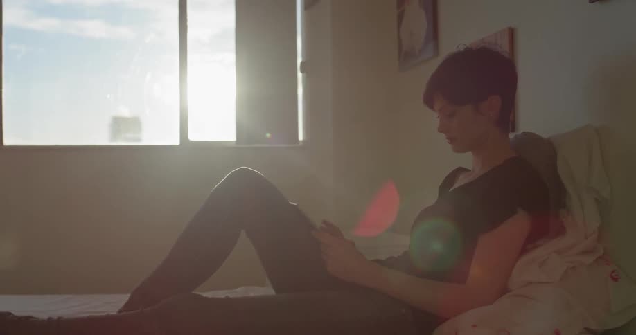 A woman uses a tablet while sitting in bed