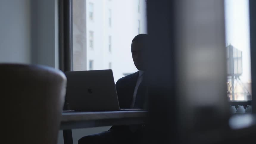 Man sits at a table in an office typing on a laptop