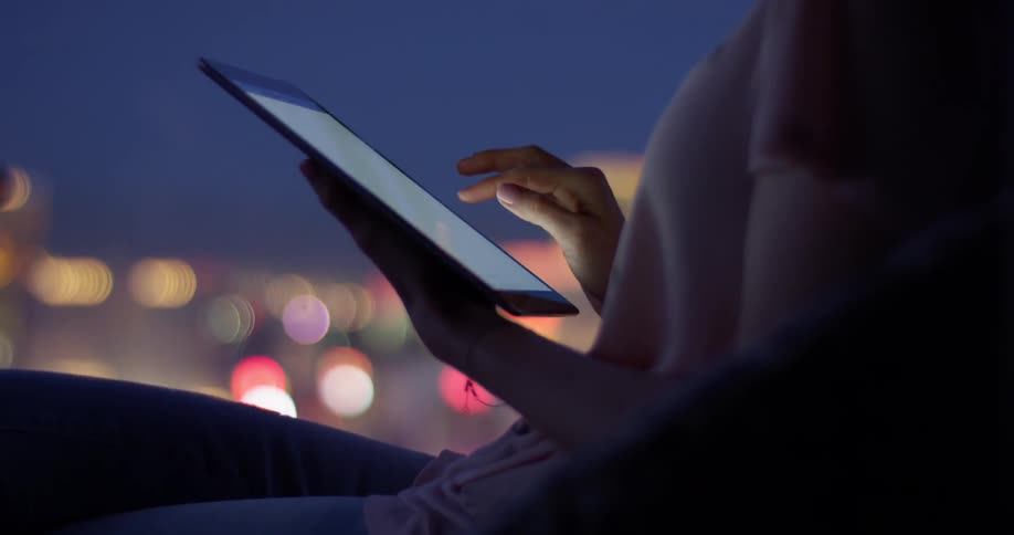Woman scrolls on her tablet as she stands under the night sky