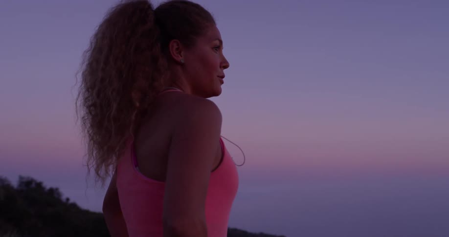 Woman stands looking out at a large body of water at sunset