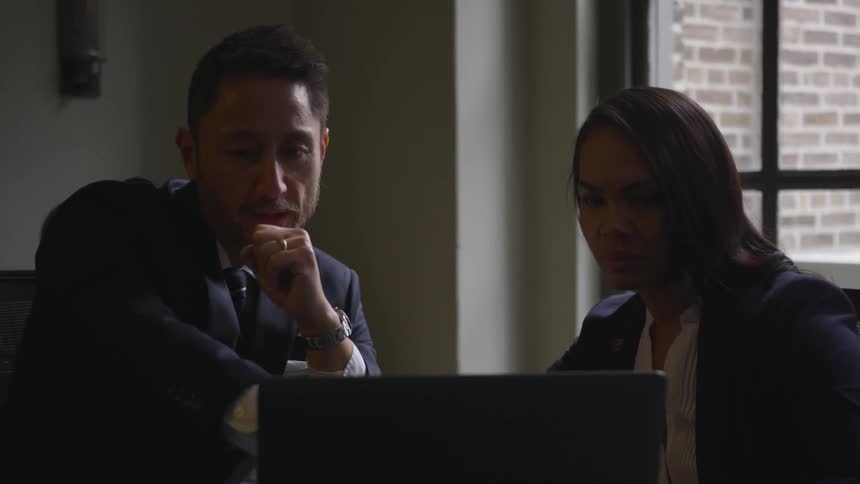 A man points at a laptop screen while talking to a woman