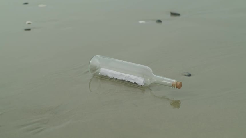 A glass bottle with a note inside sits on a sandy beach