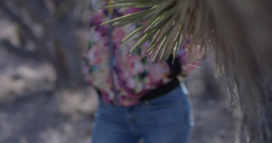 A woman stands next to a plant in a desert