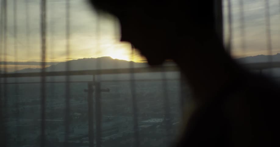 The woman stands in the dark room as the sun sets outside