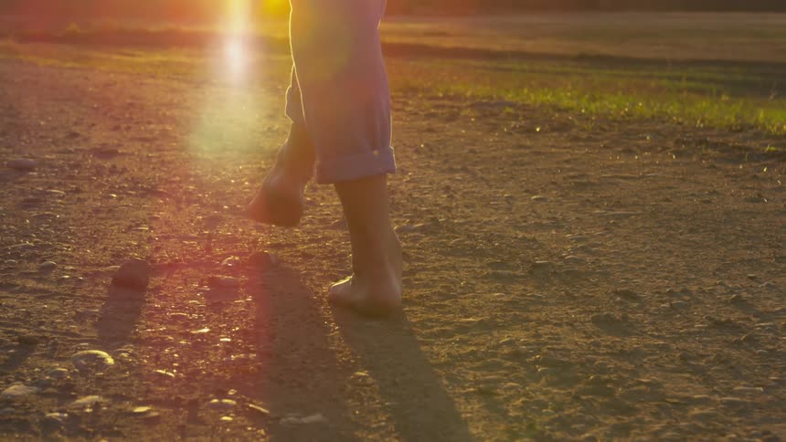 Woman walks barefoot in a field under the bright sun