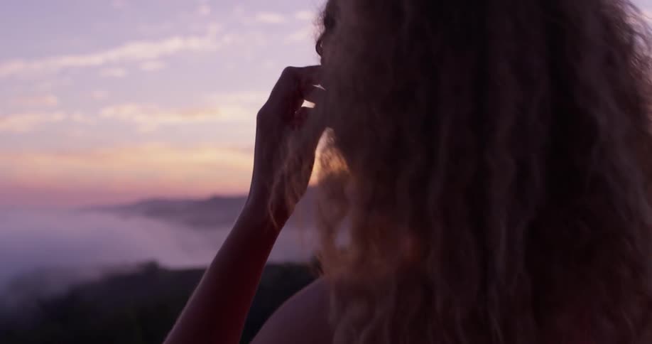 A woman walks towards the mountain side and removes her headphones