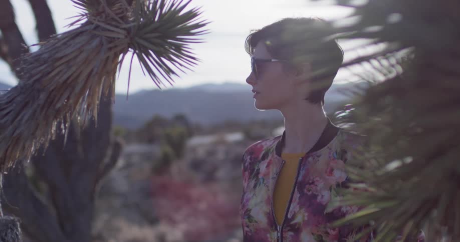 A woman stands in the desert as vehicles pass by