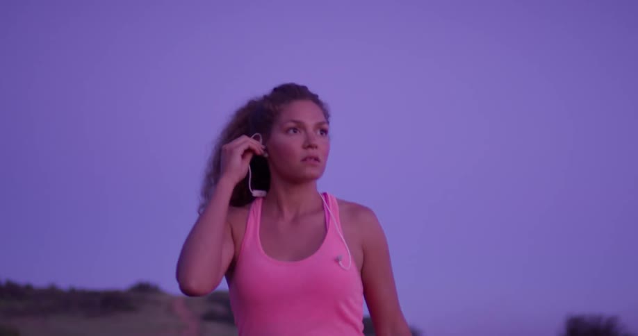 A woman walks at sunset and puts her headphones on