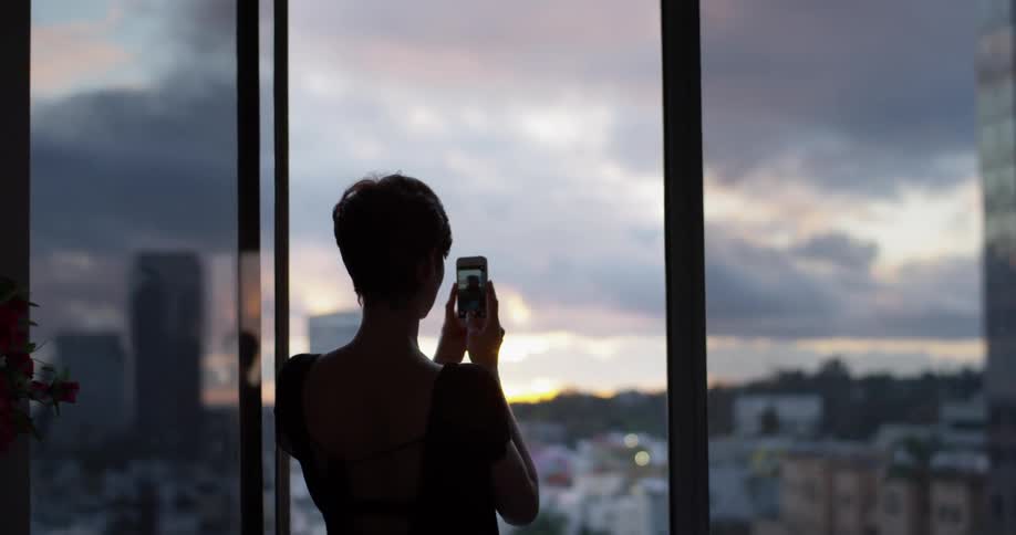 A woman takes a picture from a hotel balcony at sunset