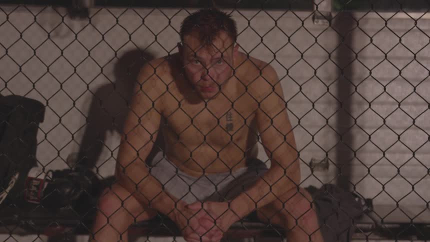 Man sits behind a chain link fence on a bench