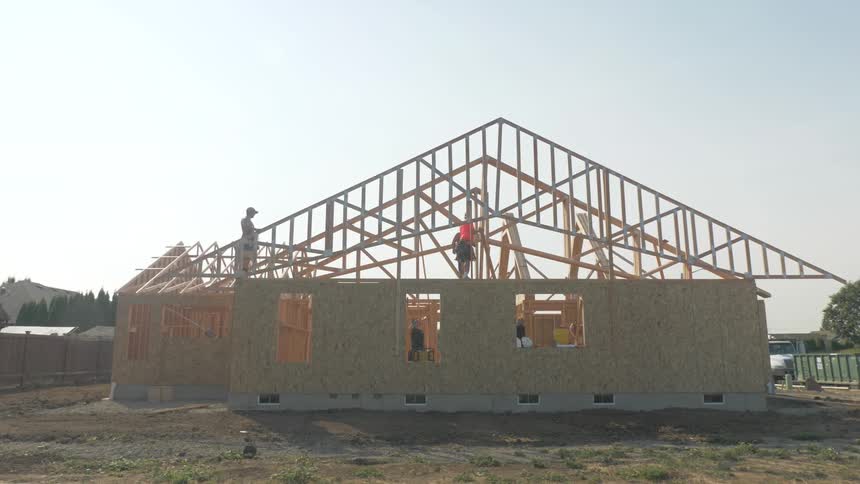 Construction workers are placing roof joists on a building in daylight
