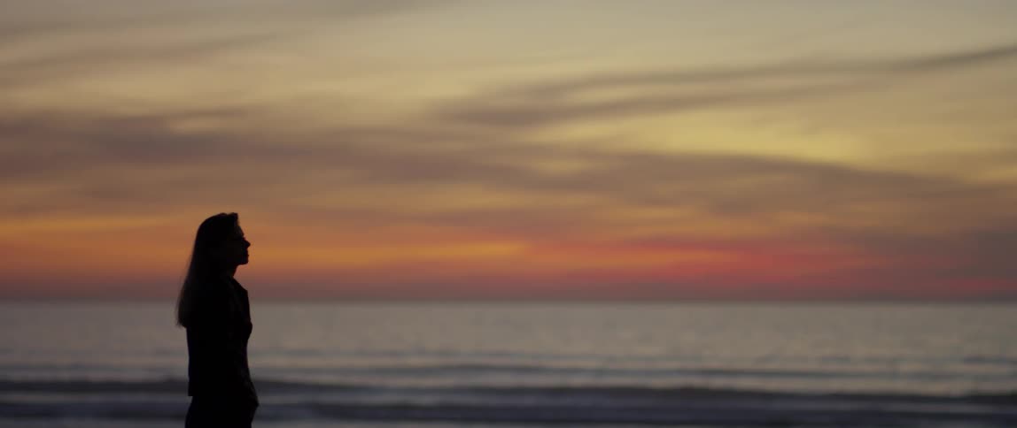 Woman stands on the beach at sunset looking up