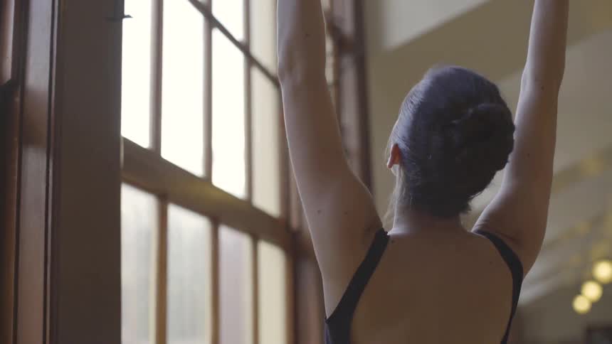 A ballerina practices next to a window