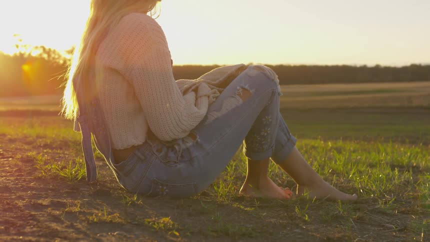 A woman is sitting on the grass at sunset