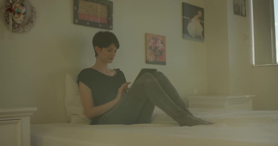 A woman uses a tablet while sitting in bed