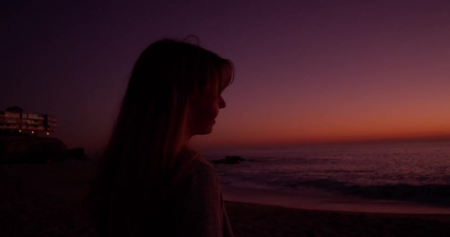 Woman smiles as she looks out at the ocean at sunset