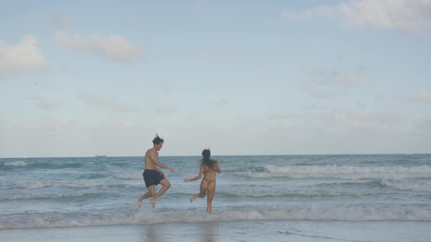 A couple hold hands running into the waves