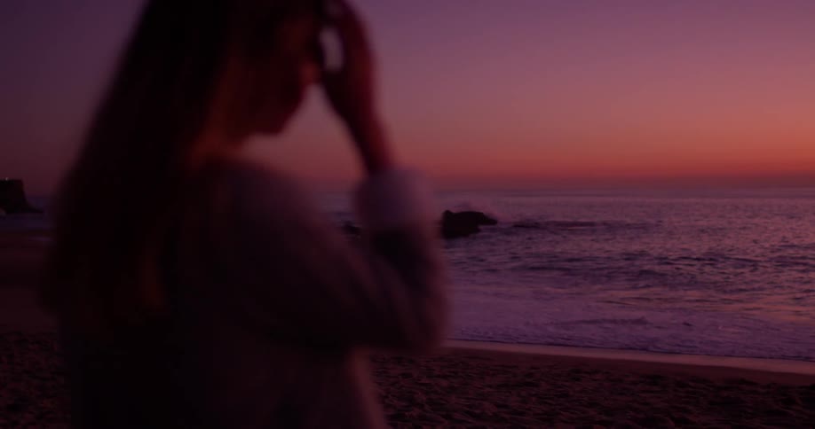Woman stands on the beach at sunset looking out
