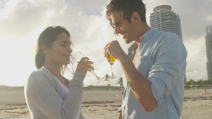 A couple clink glasses before drinking on the beach