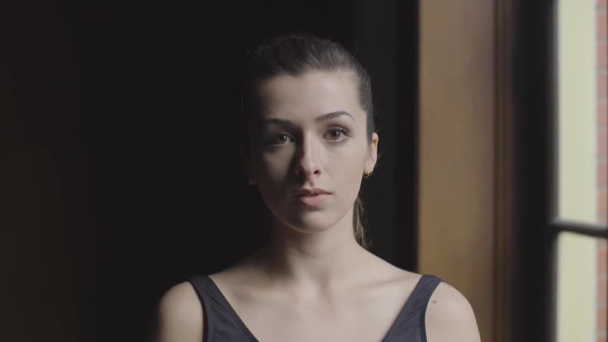 Ballerina is standing in room by window and staring in front of her