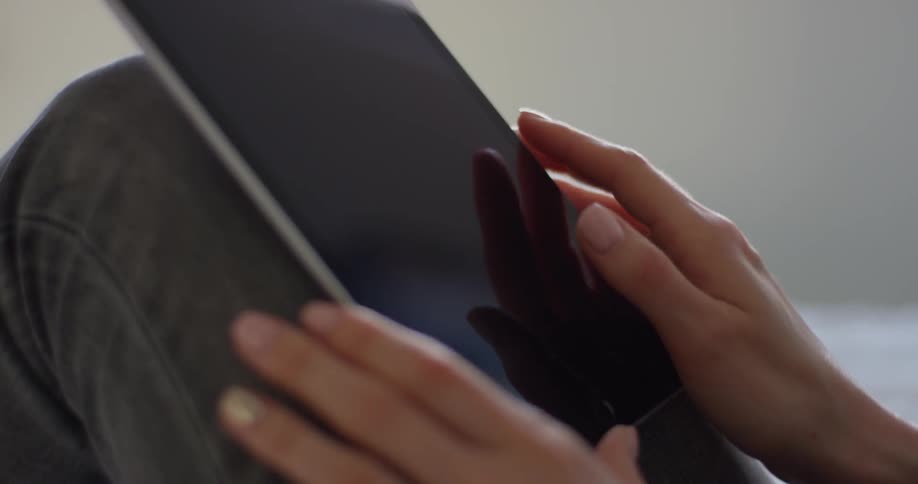 A woman scrolls on a tablet resting on her legs