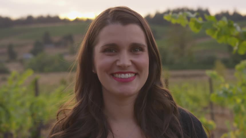 A woman smiles while standing in a vineyard