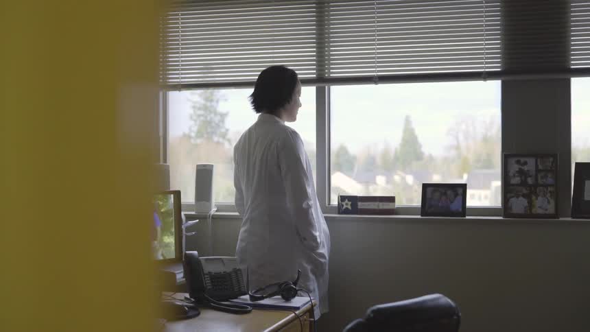 Woman in a white coat looks out her office window