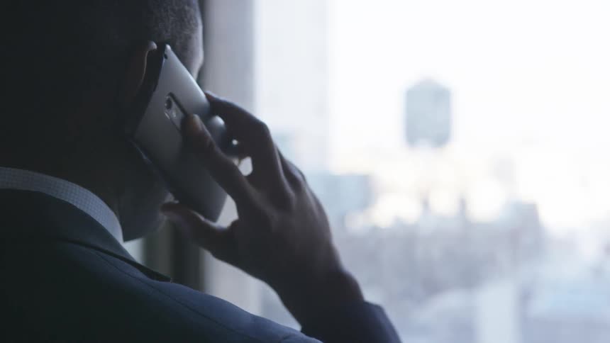 A businessman talks on a phone while looking out a window