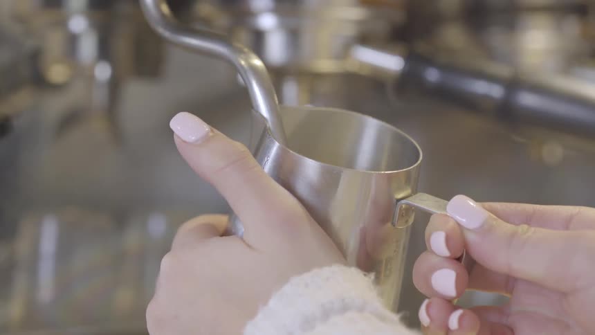A barista in a coffee shop is making steamed milk for a coffee