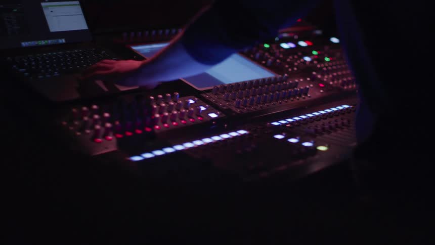 A person is turning the dials on the soundboard