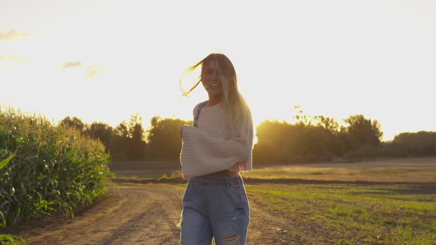 A woman smiles while walking on a farm at sunset