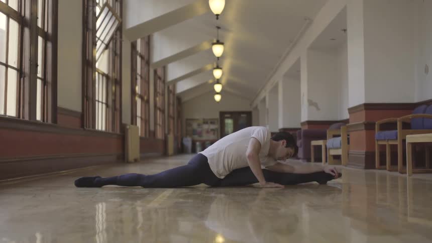 A man stretches on the floor in a long hallway