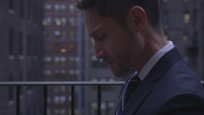 A businessman stands on a balcony in a city