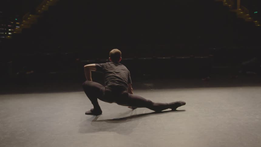 A man stretches on the dark stage