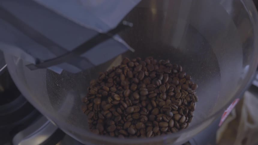 Coffee beans are poured into the cone of a funnel
