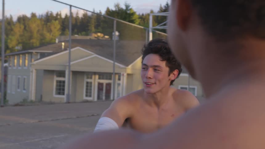 Shirtless men smile and laugh on an outdoor basketball court