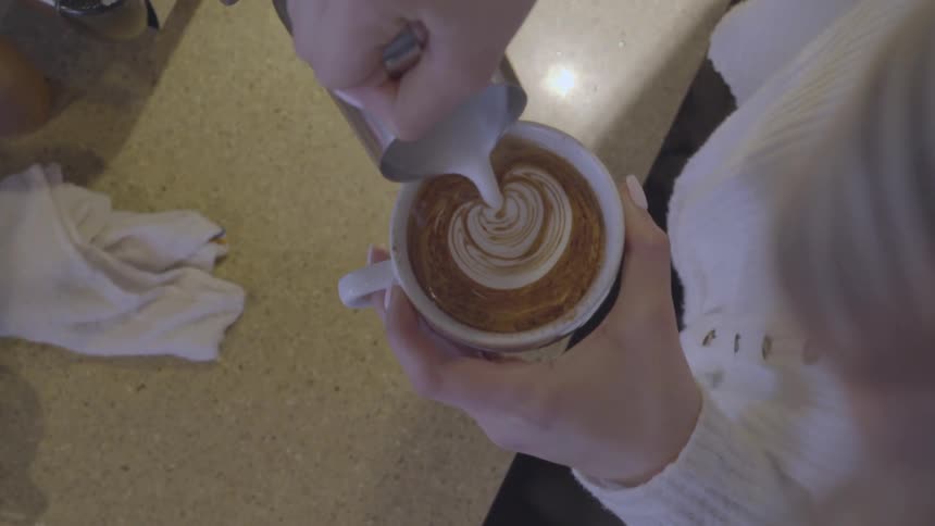 A barista is pouring cream into a cappuccino in the form of a heart