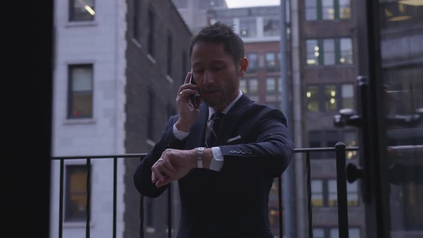 A businessman looks at his watch while talking on a phone