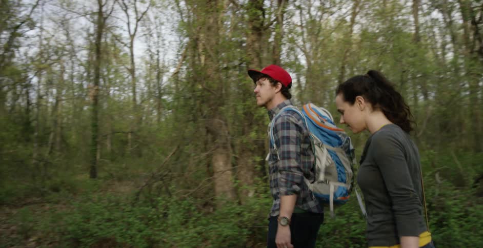 A man and woman laugh and talk while walking in the woods
